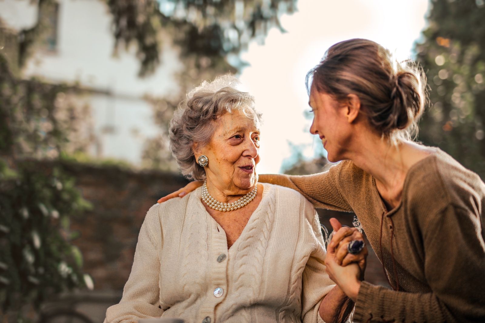 Filha adulta conversando e sorrindo com a mãe idosa em um jardim